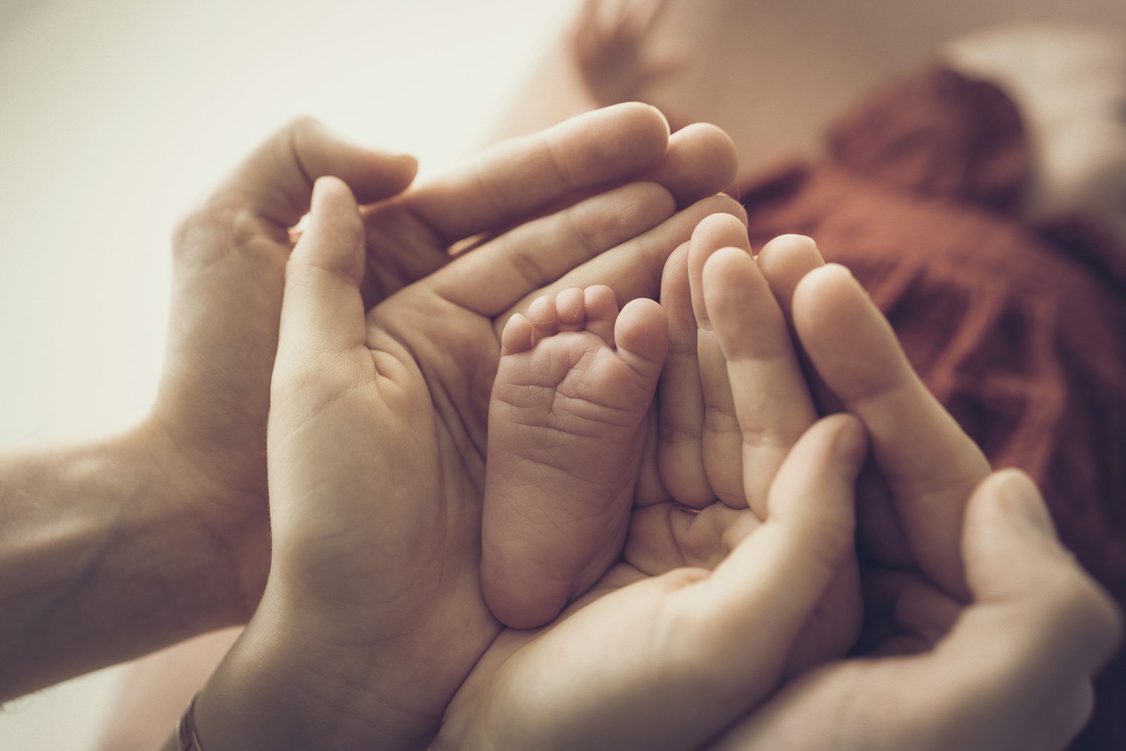 Mãos adultas segurando o pé de um recém-nascido.